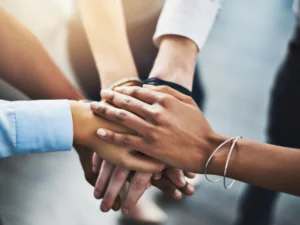 A picture of 5 people's hands - one on top of the other - signifying a pact or commitment.
