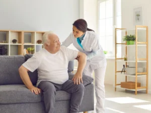 A woman helping a man stand up, by placing her arm under his.
