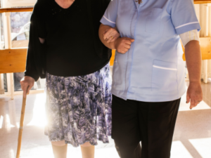 A carer helping an elderly lady to walk by linking arms.