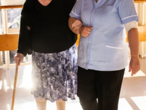 A carer helping an elderly lady to walk by linking arms.